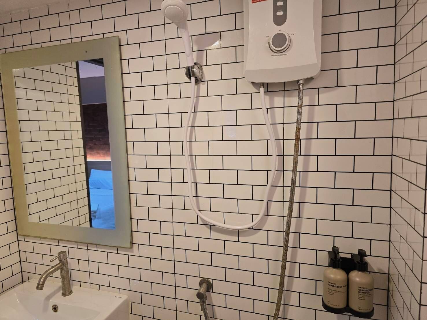 Un bagno con pareti rivestite di piastrelle bianche, uno specchio, un lavandino e un soffione doccia a mano.