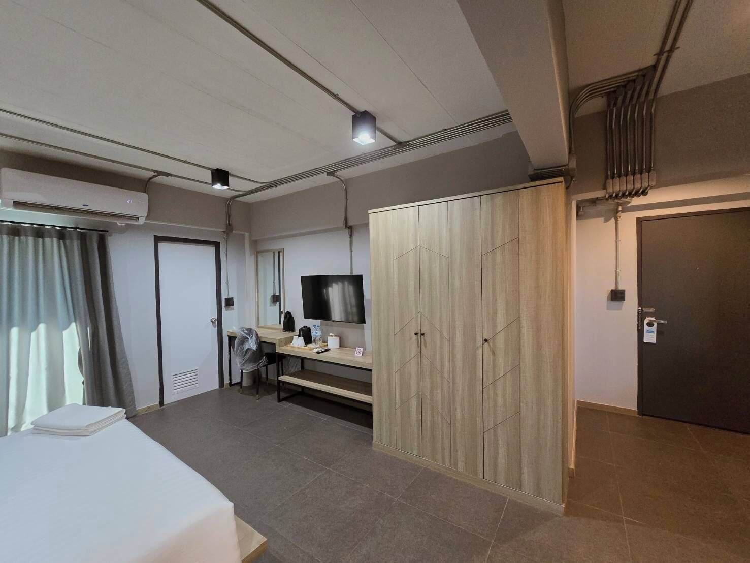 A modern hotel room with a bed, a desk, a TV, and a wardrobe.