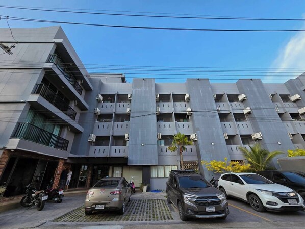 A multi-story residential building with balconies, parked cars, and a clear sky.