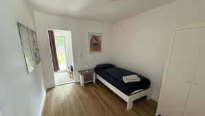 A small, bright room with a bed, a nightstand, a wardrobe, and a door leading to an outdoor area. - 3-bed apartment with kitchen & bathroom | Pension Kalifornia (NH) (Osterholz-Scharmbeck)