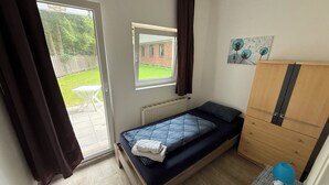 A bedroom with a bed, a radiator, a window, a wardrobe, and a small table with a lamp. - 3-bed apartment with kitchen & bathroom | Pension Kalifornia (NH) (Osterholz-Scharmbeck)