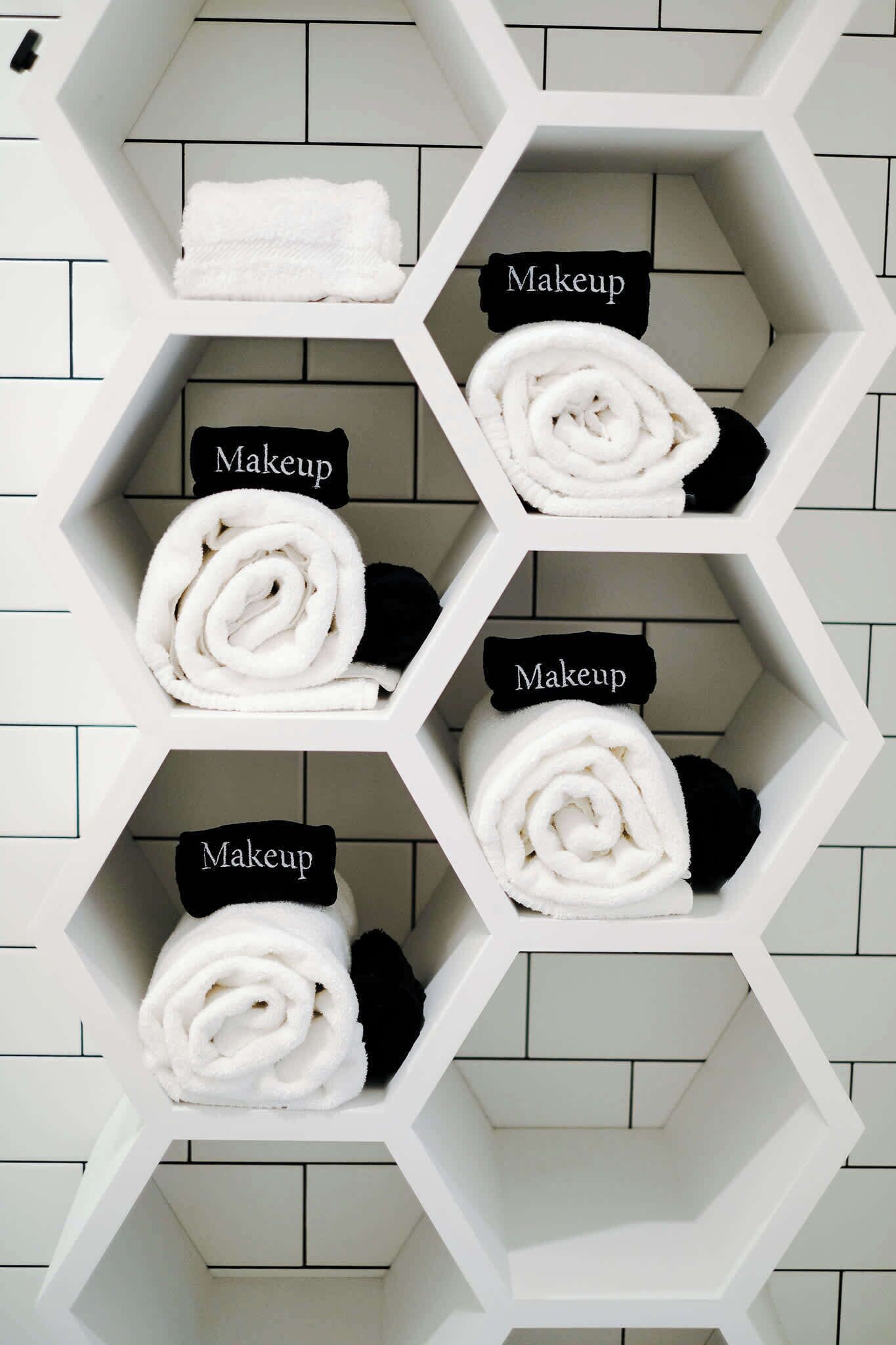 Un baño con estantes hexagonales que contienen toallas enrolladas y la etiqueta 'Maquillaje'.