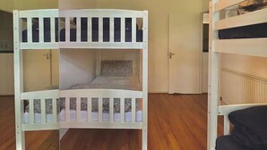 Ein Zimmer mit zwei Etagenbetten, Holzboden, einer weißen Tür und einer Deckenleuchte.