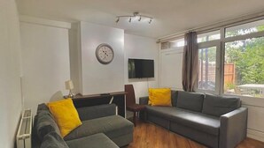 Ein modernes Wohnzimmer mit einer Eckcouch, einem Flachbildfernseher und einem großen Fenster mit Vorhängen.