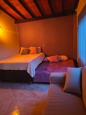 A room with two beds, a sofa, and a wooden ceiling. - Hostal Pacífico Encanto (Medellin)
