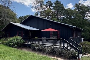 A two-story building with a dark exterior, a red umbrella on the porch, and a staircase leading to the upper level. - Cozy Getaway at Two Willows Horse Farm, near Lake Glenville, Highlands, Cashiers (Cullowhee)