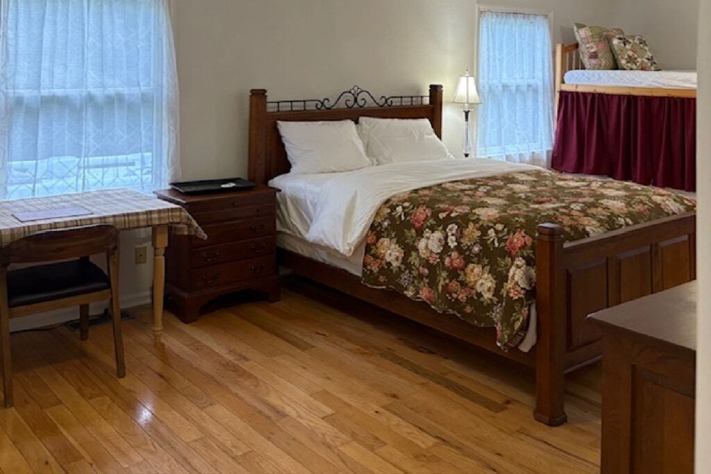 A bedroom with a wooden bed, a nightstand, a desk with a chair, and a window with curtains.