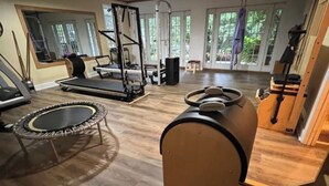 Ett hemmagym med en studsmatta, träningsutrustning och ett stort fönster med utsikt över naturen.