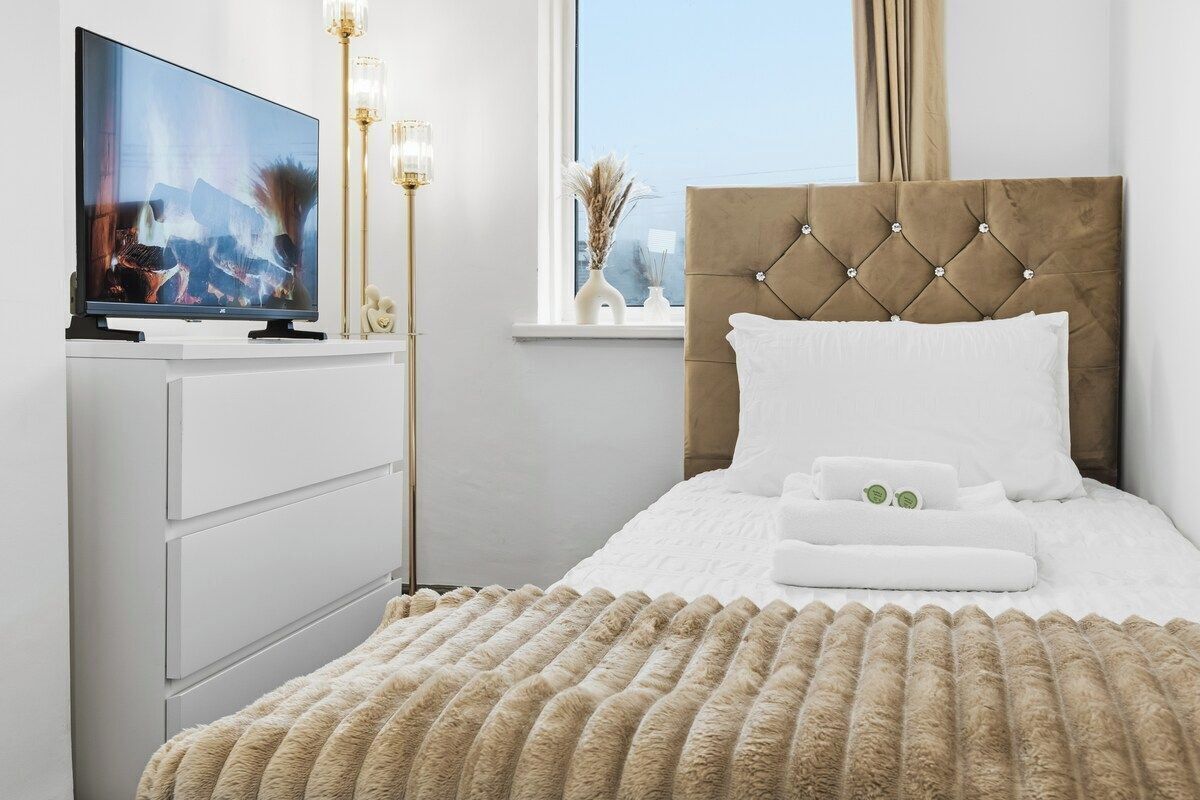 A hotel room with a bed, a television, a bedside table, and a window.