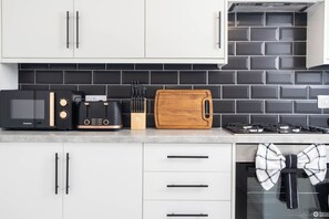 A kitchen with a microwave, toaster, wooden cutting board, and a gas stove. - Haydock WA11 | Large 4 BR Home | Work & Group Stay (Haydock)