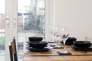 A dining table set with black bowls and wine glasses, positioned near a glass door with a view of a garden. - Haydock WA11 | Large 4 BR Home | Work & Group Stay (Haydock)