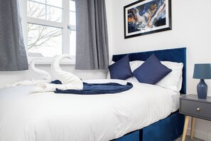 Ein ordentlich bezogenes Bett mit blauem Kopfteil, weißen Kissen und einer dunkelblauen Decke.
