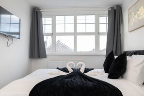 A bedroom with a bed, a television mounted on the wall, and a window with curtains. - Haydock WA11 | Large 4 BR Home | Work & Group Stay (Haydock)