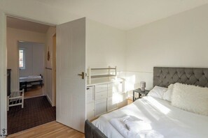 Ein Schlafzimmer mit einem Bett, Nachttischen, einem Kleiderschrank und einer Tür zu einem anderen Raum.