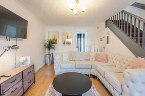 Ein Wohnzimmer mit Ecksofa, rundem Couchtisch, Wandfernseher und einer Treppe.