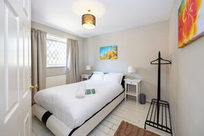 A hotel room with a bed, bedside tables, a lamp, a coat rack, and a window with curtains. - Modern 3BR Home | Parking | Heart of West Didsbury (Manchester)