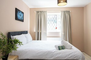 A hotel room with a bed, a window with curtains, a bedside plant, and a painting on the wall. - Modern 3BR Home | Parking | Heart of West Didsbury (Manchester)