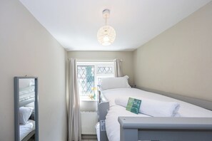 A hotel room with a bunk bed, a bedside table, a mirror, and a window with curtains. - Modern 3BR Home | Parking | Heart of West Didsbury (Manchester)