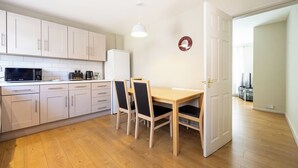 A compact kitchen with white cabinets, a microwave, and a coffee maker. There is a dining table with chairs and a pendant light. - Modern 3BR Home | Parking | Heart of West Didsbury (Manchester)