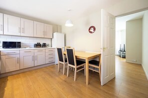 A compact kitchen with white cabinets, a microwave, and a coffee maker. There is a dining table with chairs and a pendant light. - Modern 3BR Home | Parking | Heart of West Didsbury (Manchester)