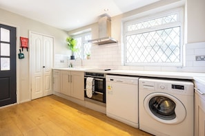 A kitchen with a washing machine, oven, and a fire blanket on the wall. - Modern 3BR Home | Parking | Heart of West Didsbury (Manchester)