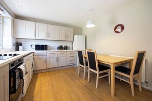 Une cuisine compacte avec des meubles blancs, un four à micro-ondes, une machine à café et une table à manger avec des chaises.