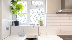 A kitchen with a window, a sink, a stove, and potted plants. - Modern 3BR Home | Parking | Heart of West Didsbury (Manchester)