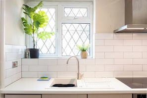 A kitchen with a window, a sink, a stove, and potted plants. - Modern 3BR Home | Parking | Heart of West Didsbury (Manchester)