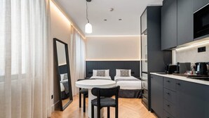 Une chambre d’hôtel moderne avec une table à manger ronde, deux lits, une cuisine intégrée et un grand miroir.