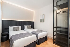 Moderni hotellihuone, jossa on kaksi sänkyä, yöpöytä, vaatekaappi ja henkarikaappi.