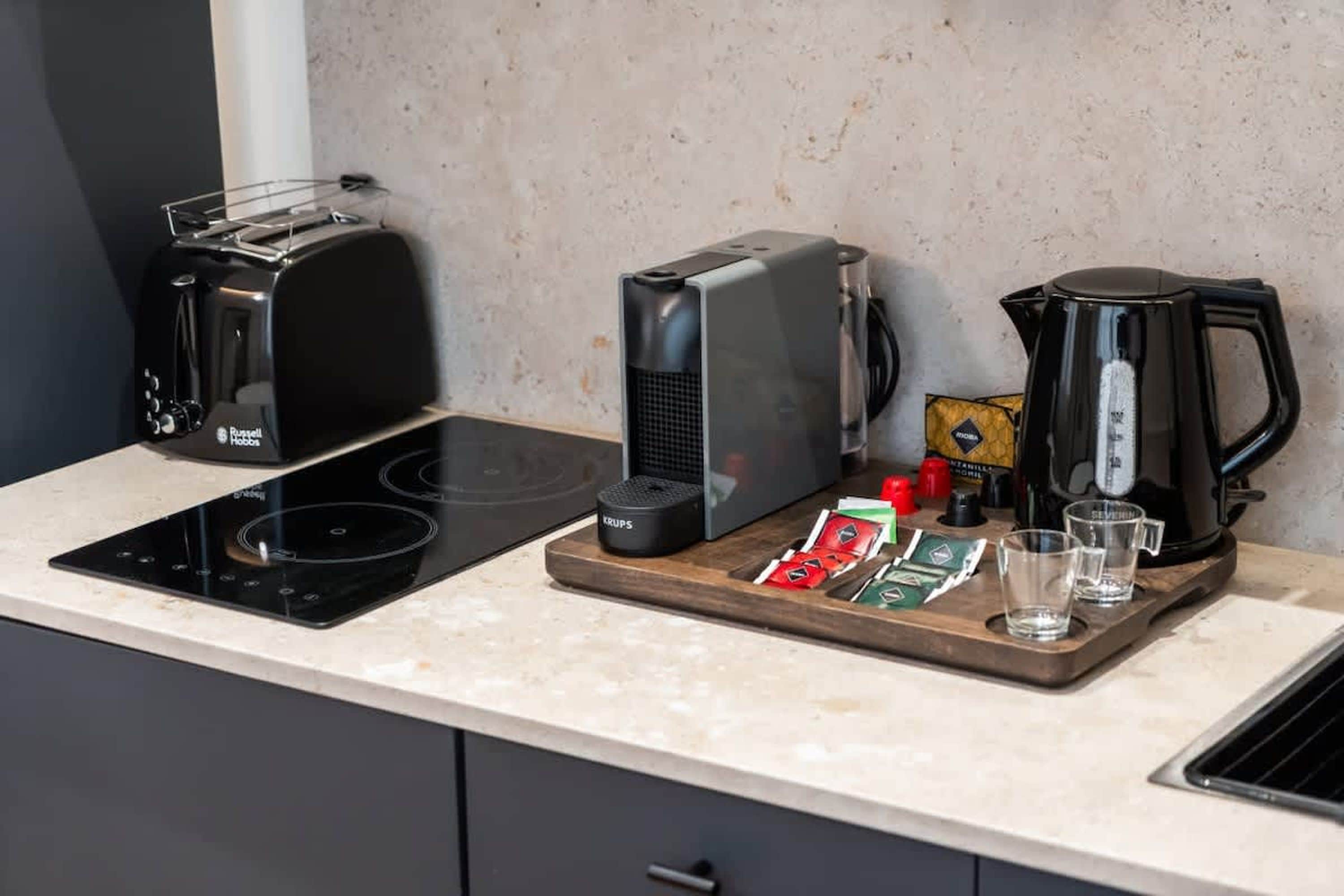 Una cucina con un tostapane nero, una macchina da caffè, un bollitore e un vassoio di legno con tazze e condimenti.