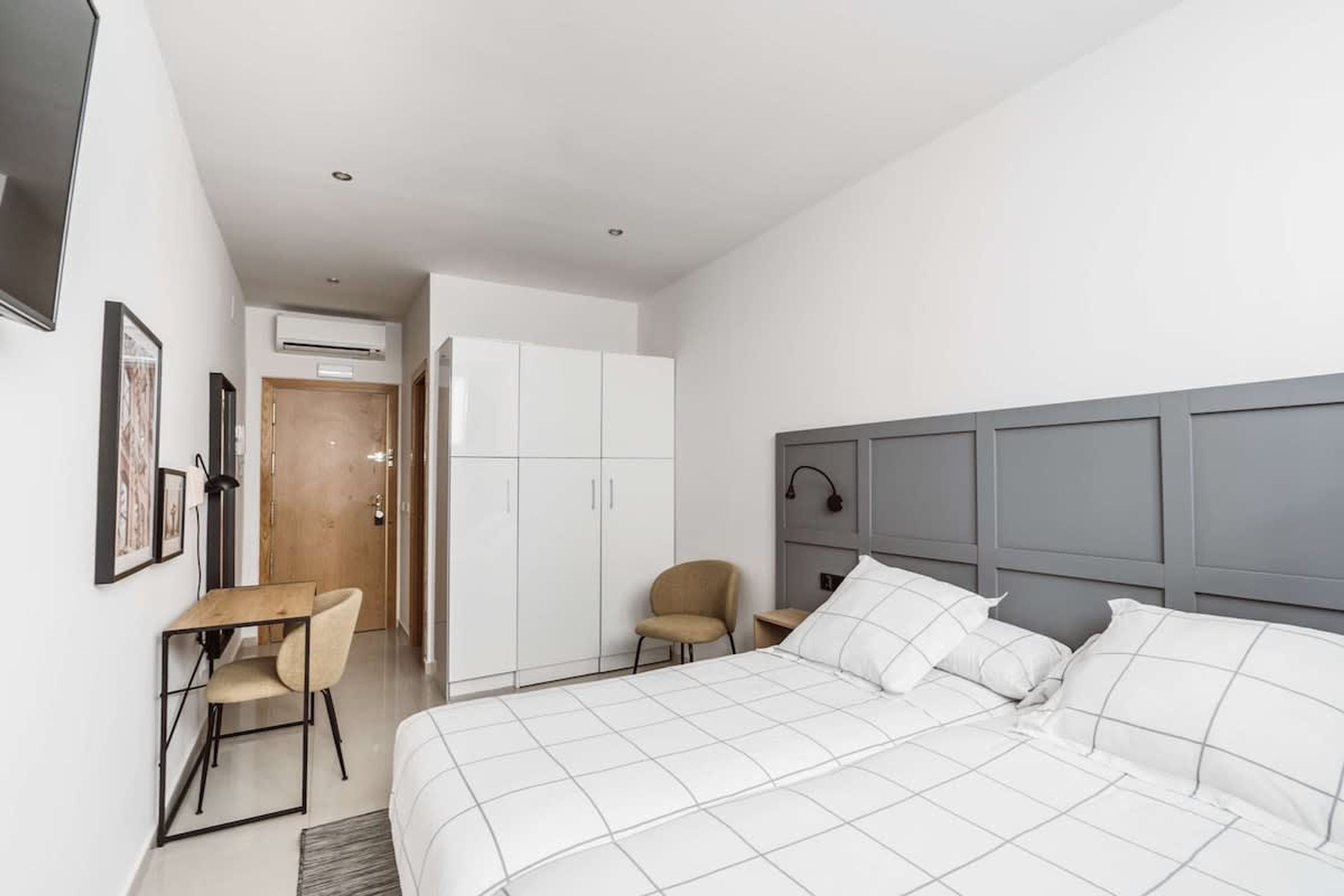 Une chambre d’hôtel moderne avec un grand lit, un bureau et une chaise. On y trouve également une armoire et un appareil de climatisation fixé au mur.