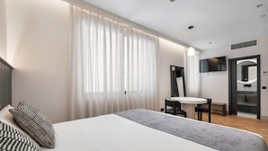 Une chambre d’hôtel moderne avec un grand lit, une petite table et un téléviseur.
