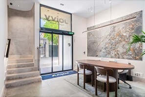 Un hall d’hôtel moderne avec un grand mur de marbre, une table de conférence en bois et un escalier.