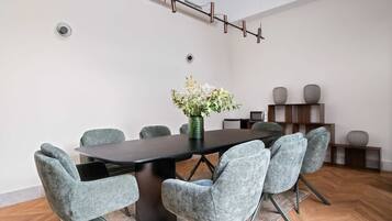 Una sala de conferencias con una mesa oscura, sillas tapizadas de gris, un jarrón con flores y una lámpara moderna.