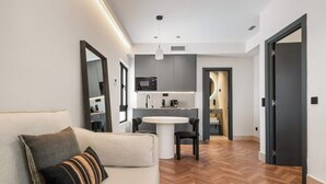 A modern living room with a sofa, a round table, and a kitchen area in the background. - Pac Fico Suite With Double Sofa Bed Near Retiro (Madrid)