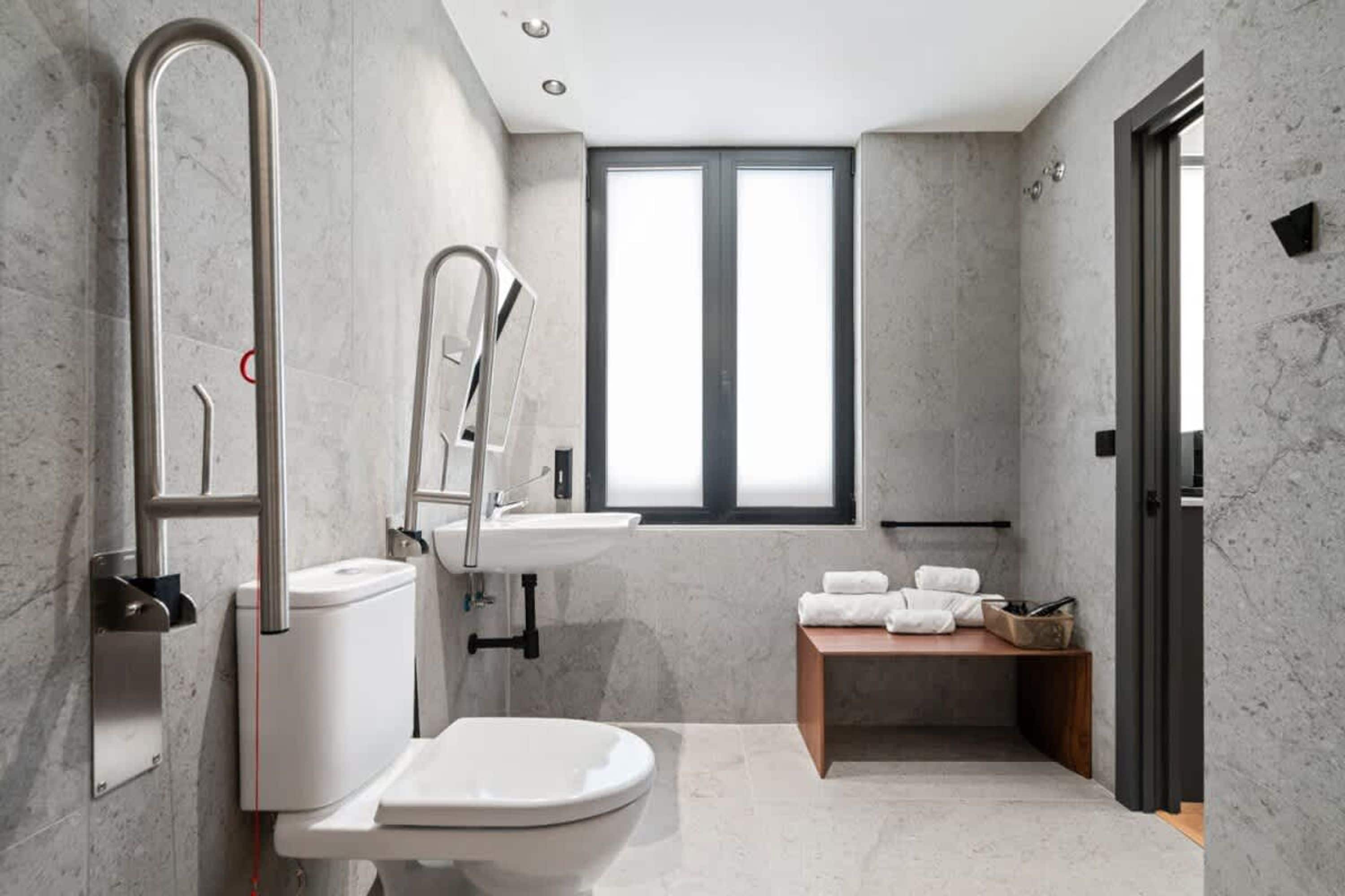 Un baño moderno con inodoro, bidé y lavamanos, paredes de mármol y una ventana que proporciona luz natural.