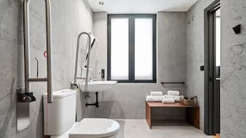 Un baño moderno con inodoro, bidé y lavamanos, paredes de mármol y una ventana que proporciona luz natural.