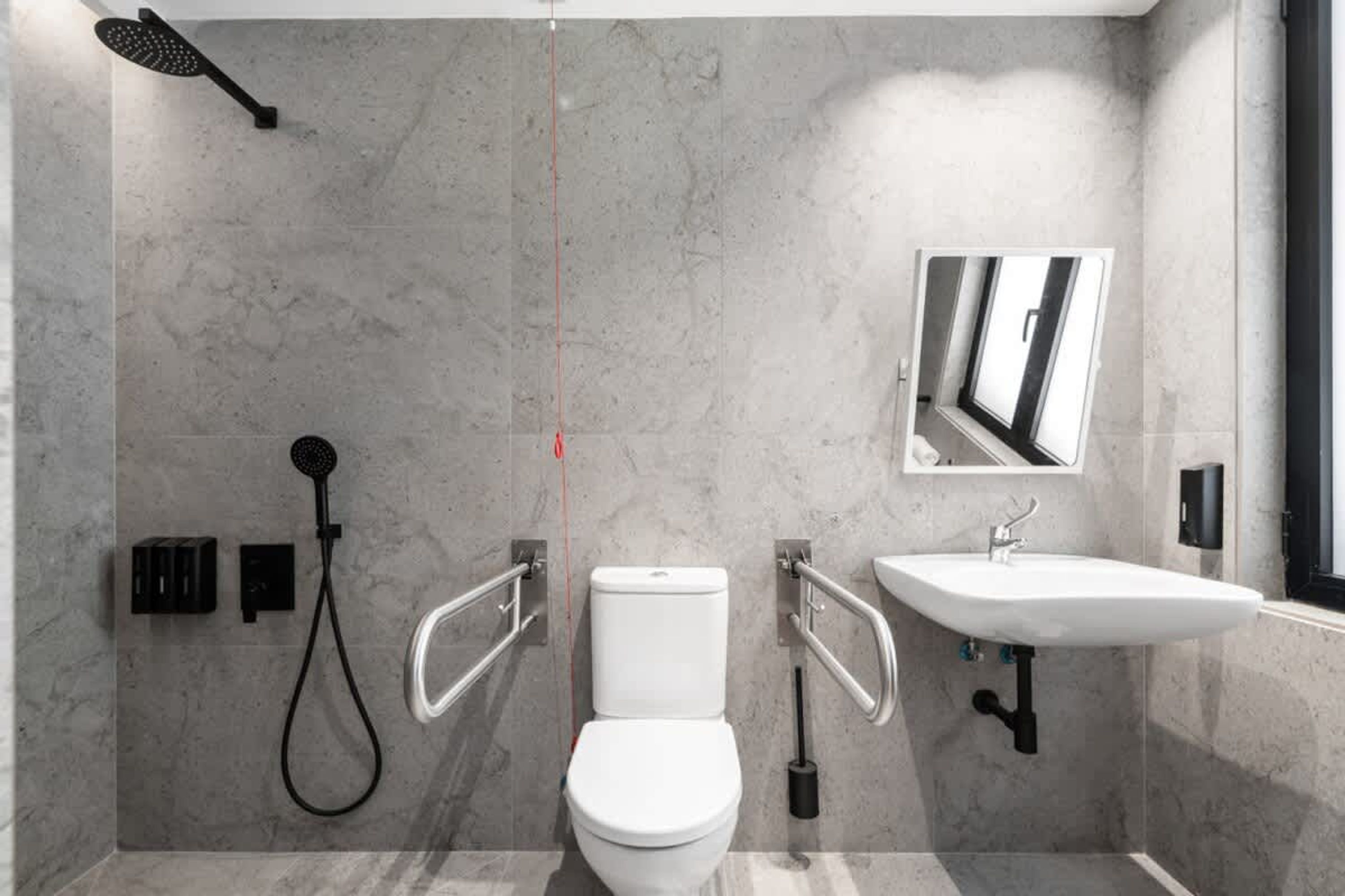 A modern bathroom with a toilet, bidet, and sink, equipped with handrails and a showerhead.