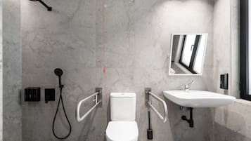 A modern bathroom with a toilet, bidet, and sink, equipped with handrails and a showerhead.