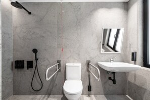 Un baño moderno con inodoro, bidé y lavamanos, equipado con barras de apoyo y ducha.