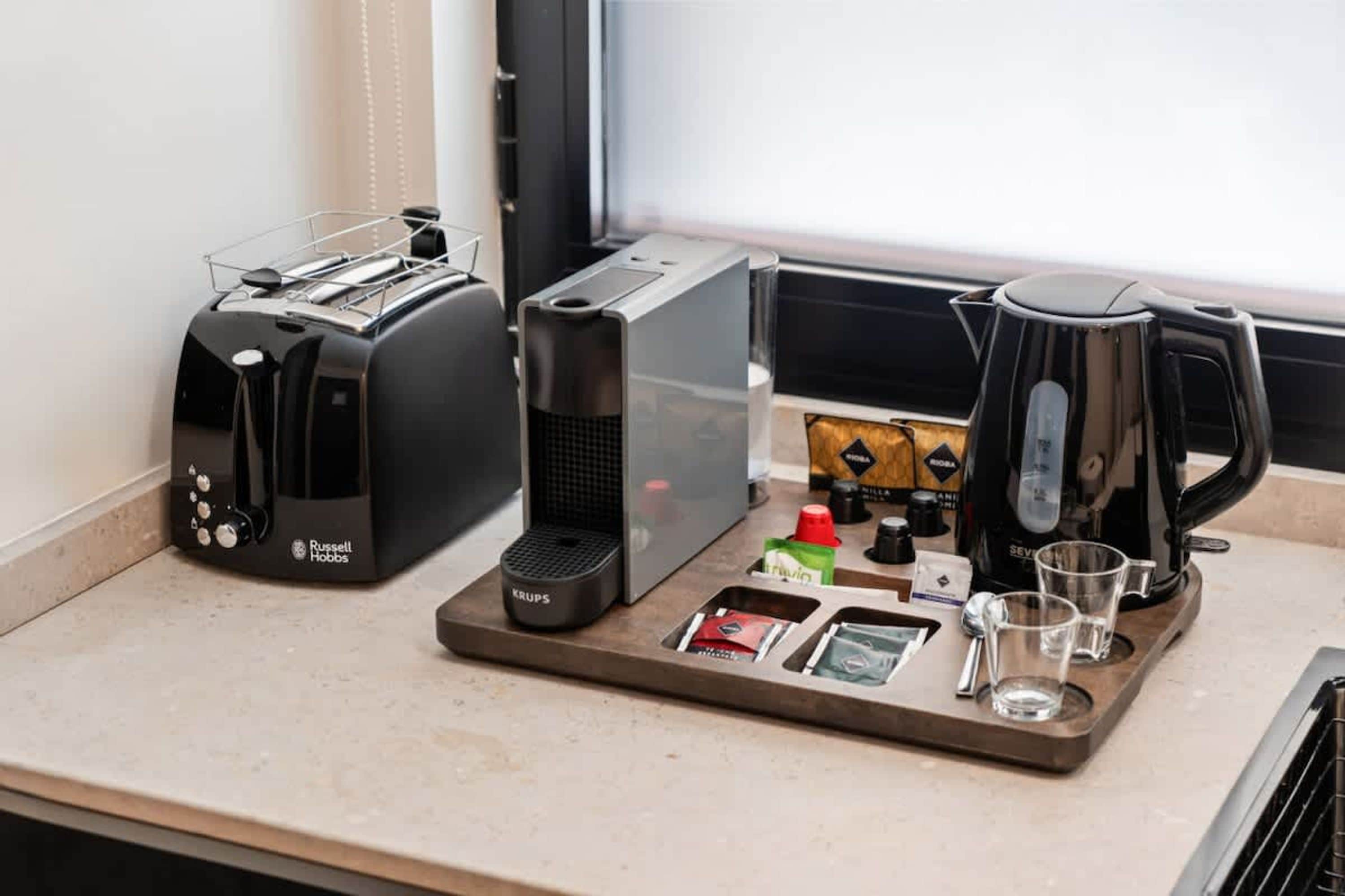 A kitchenette with a toaster, a coffee maker, and a tray with coffee pods, a kettle, and glasses.
