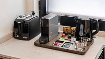 A kitchenette with a toaster, a coffee maker, and a tray with coffee pods, a kettle, and glasses.