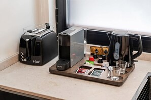 Una kitchenette con tostadora, cafetera y una bandeja con cápsulas de café, hervidor y vasos.