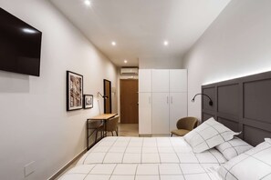 Een slaapkamer met een bed, een bureau, een stoel, een kledingkast en een televisie aan de muur.