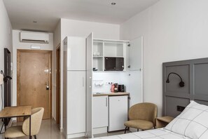 Een kleine kamer met een bed, een kitchenette met een magnetron, een stoel en een bureau.