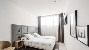 Una habitación de hotel moderna con cama, sillón, televisión y cuadros en la pared.