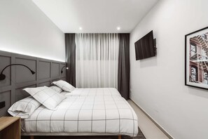 Een moderne hotelkamer met een groot bed, een flatscreen televisie aan de muur en een raam met dunne gordijnen.