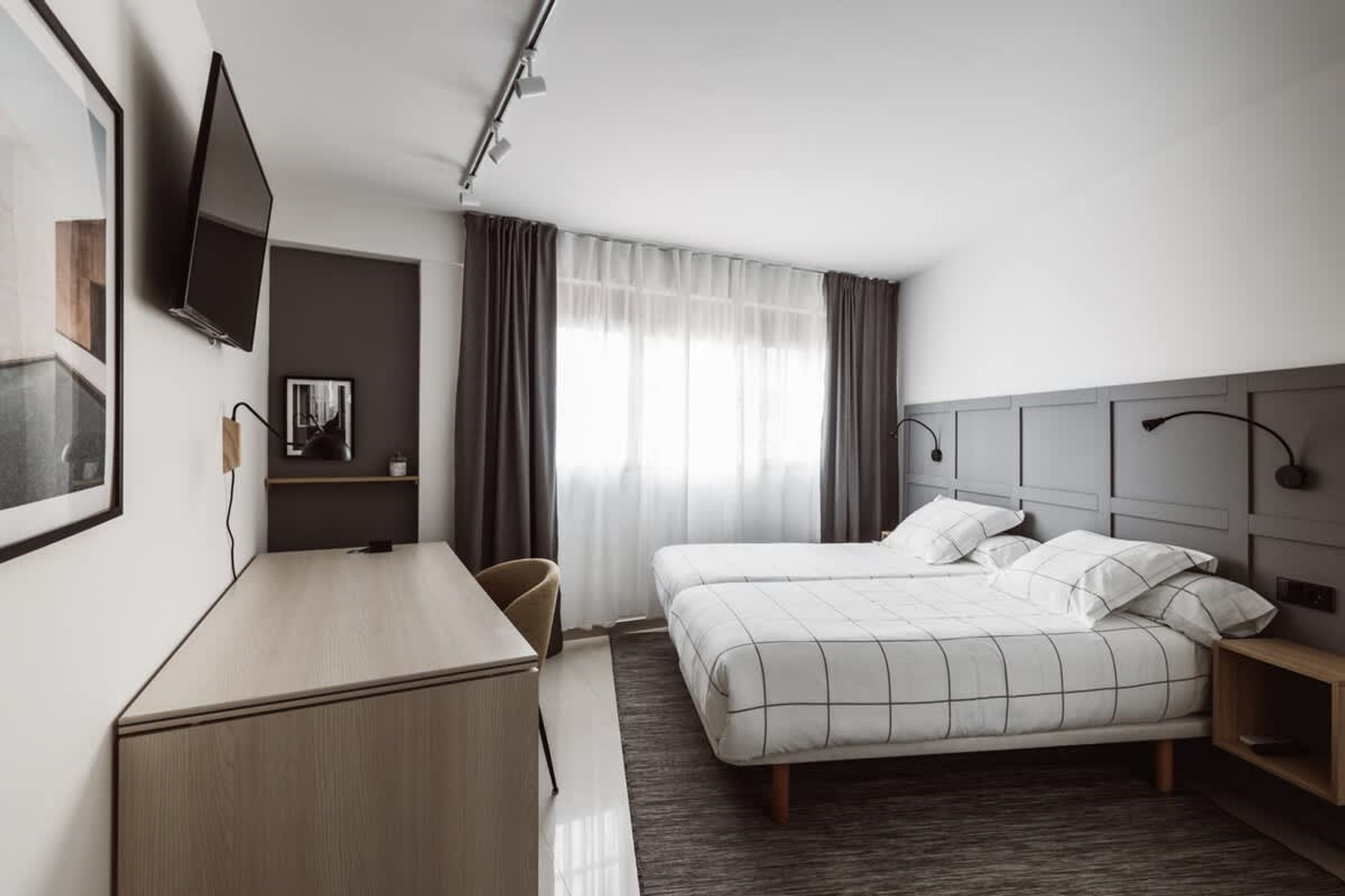 Une chambre d’hôtel moderne équipée d’un lit, d’un bureau, d’une chaise et d’un téléviseur fixé au mur.