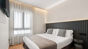 A modern bedroom with a large bed, a bedside table, and a wall-mounted TV. - Pac Fico Suite With Single Sofa Bed Near Retiro (Madrid)